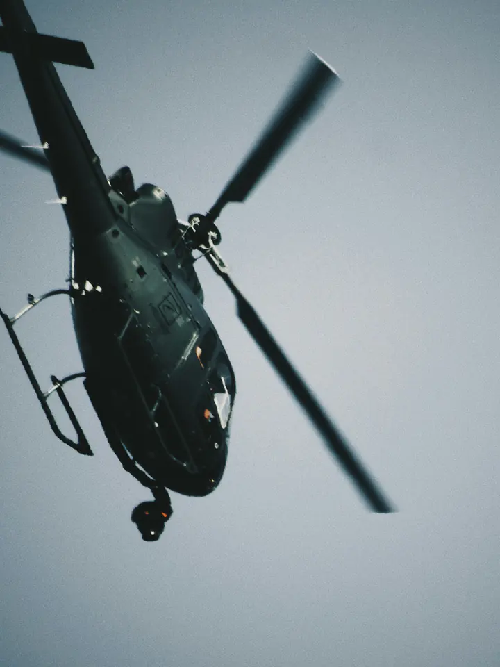A black helicopter banking overhead, seen from below