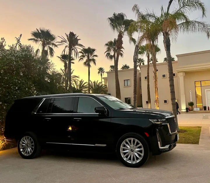 Cadillac Escalade at dusk outside a villa entrance, among palm trees